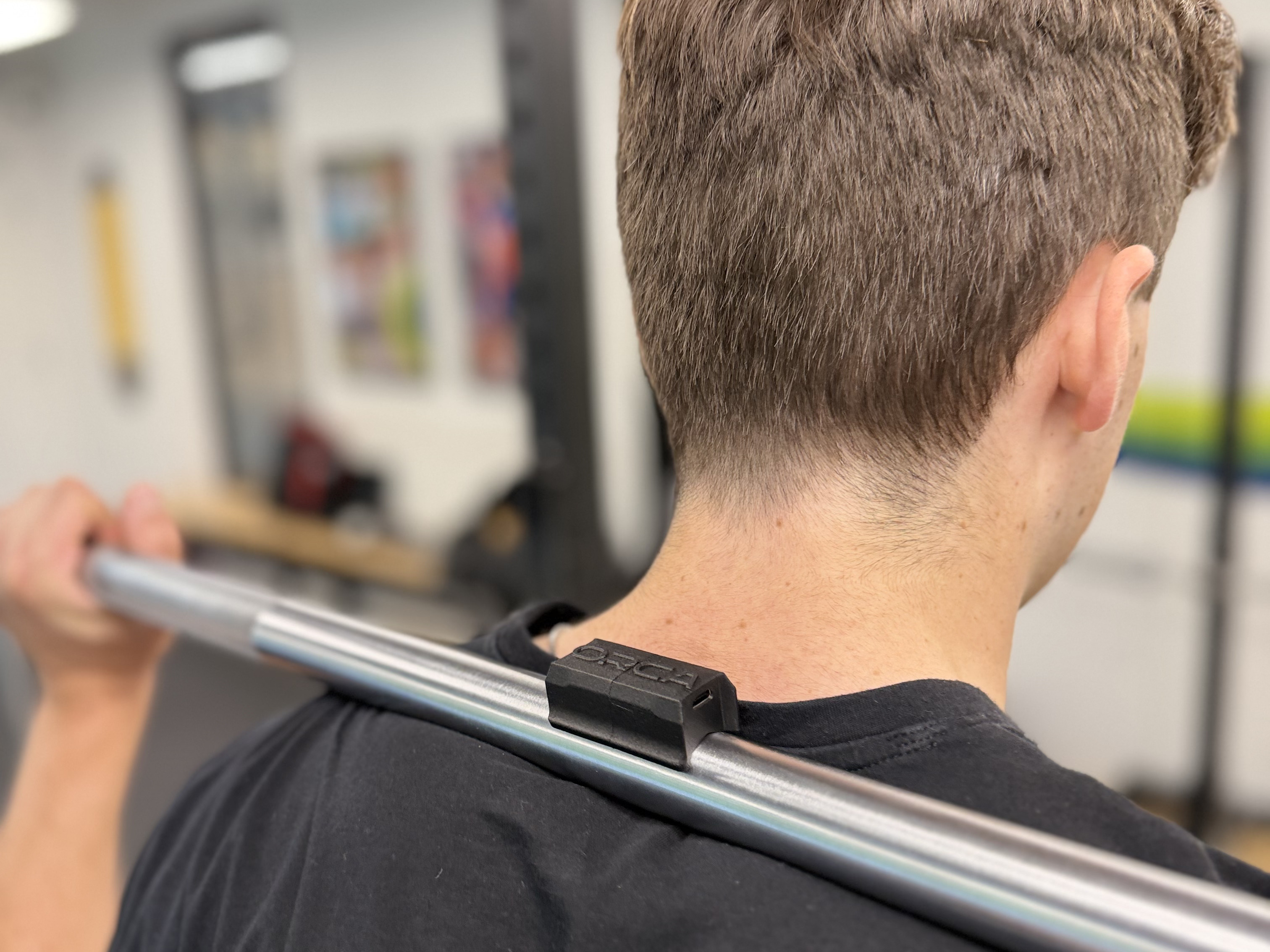 Athlete with an ORCA sensor clipped to a barbell across their shoulders